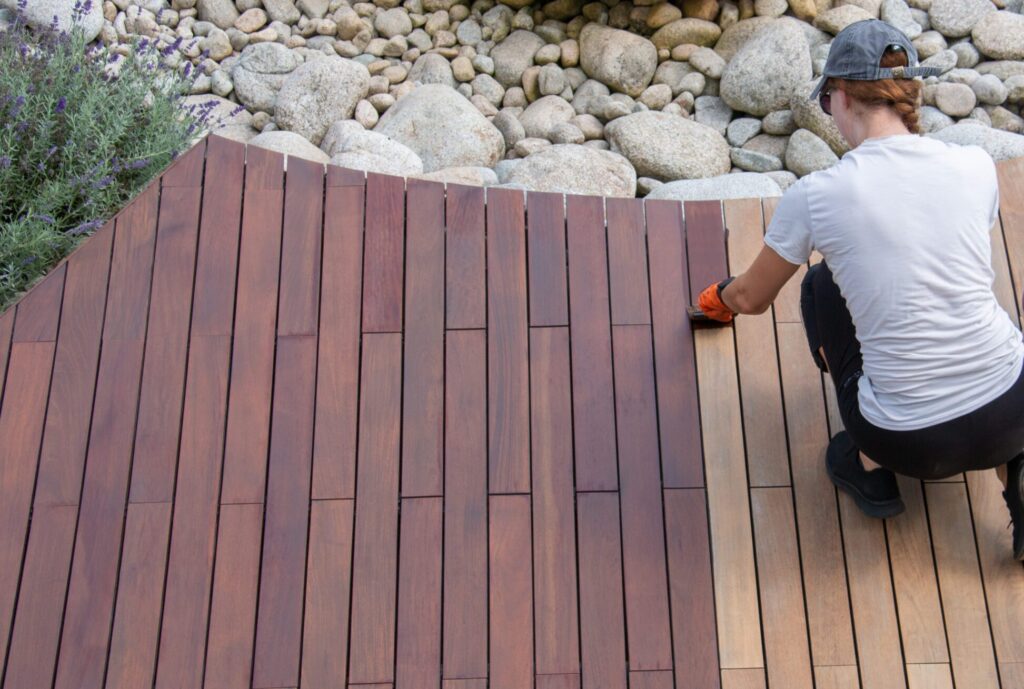 Hardwood deck oil application, overhead woman painting wood boards of garden decking